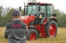 Mężczyzna w polarze z napisem ”Belarus Tractors”, w tle czerwony ciągnik MTZ Belarus.