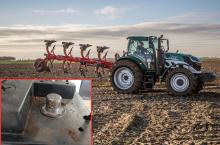 Ciągnik na polu z podniesionym pługiem 4-skibowym. Na pierwszym planie słupek akumulatora do ciągnika.