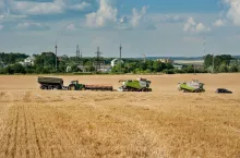 Kombajny zbożowe oraz ciągnik z przyczepą podczas zbioru zbóż na dużym polu uprawnym.