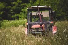 Stary traktor sfotografowany podczas postoju na łące lub polu, w otoczeniu wysokiej trawy. Zdjęcie przedstawia autentyczną scenę z polskiej wsi, z charakterystycznym dla lata bujnym otoczeniem roślinnym.