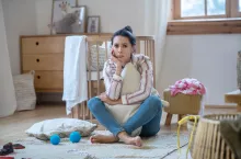 At home. Sad young woman hugging pillow, propping up her head, sitting on the floor